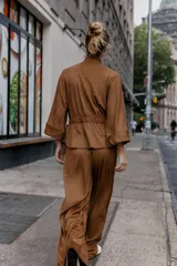 Camisa de estilo safari en color marrón con efecto ante, cuello subido y mangas anchas de largo tres cuartos con terminación en vuelta. Presenta bolsillos con solapa en el pecho, cintura ajustable con lazo del mismo tejido y cierre frontal oculto con cremallera y botones a presión.