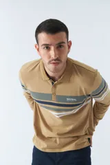 Remera tipo polo de manga larga azul marino con rayas horizontales blancas, grises y rosadas en el pecho. Tiene cuello clásico con botones y logo estampado en el pecho. Corte regular.