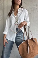 Camisa de lino color blanco, de corte holgado y manga larga con puños arremangados. Presenta cuello clásico, cierre frontal con botones y detalle de botones decorativos en el lateral inferior.