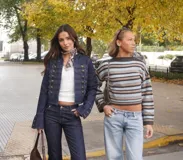 Chaqueta de denim estilo militar con diseño napoleónico, caracterizada por su doble fila de botones metálicos decorativos en el frente y mangas acampanadas con detalles de botones en los puños. Presenta un corte entallado y cuello redondo.