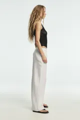 Pantalón blanco de tiro medio con pierna ancha y tejido que contiene lino. Presenta cintura con trabillas y un cinturón ajustable con lazada del mismo tejido. Cierre frontal con cremallera y botón.