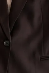 Blazer de manga corta color marrón oscuro, de botonadura sencilla con solapas de muesca, cierre de un botón, bolsillos delanteros ribeteados y forro interior.