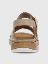 Sandalia de plataforma baja color beige con tiras cruzadas, una de ellas con acabado texturizado brillante. Presenta una tira ajustable con hebilla decorativa y cierre de velcro, sobre una suela de estilo yute con base de poliuretano.