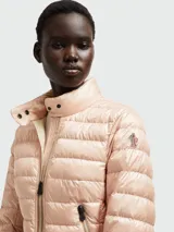 Chaqueta acolchada de plumas Moncler, modelo Walibi, en color salmón claro. Presenta cuello alto, cierre frontal con cremallera, bolsillos laterales con cierre y logo de la marca en la manga.