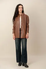 Campera estilo sobrecamisa confeccionada en cuero negro, de corte recto, con cuello camisero y cierre frontal de botones metálicos a presión.