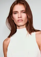 Top blanco de punto con cuello perkins, sin mangas, diseño entallado y volante en el bajo.