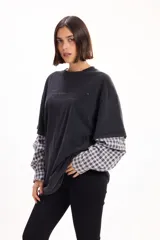 Remera oversize de jersey de algodón color negro, con diseño de doble capa que simula una camisa de cuadros incorporada en las mangas y el bajo.
