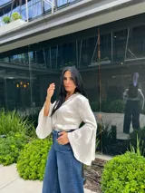 Blusa negra de manga larga con cuello camisero y puños acampanados o con aberturas.