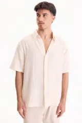 Camisa de muselina de manga corta color beige, con cuello camisero y cierre frontal de botones.