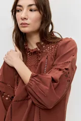 Camisa de manga larga abullonada color marrón, con detalles de bordados calados en el pecho y las mangas, y cierre frontal con botones.