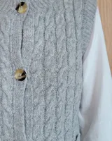 Chaleco de punto con diseño de trenzas, color gris oscuro, con cierre frontal de botones grandes y bolsillos laterales.