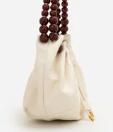 Cartera hobo marca Satinato en poliuretano color marfil, con diseño fruncido, cierre de cordón ajustable y asa rígida de esferas de madera.