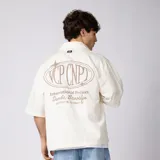 Camisa de manga corta color marfil, corte boxy, con cuello camisero, cierre frontal de botones y pequeño bordado marrón en el pecho con las siglas VCP.