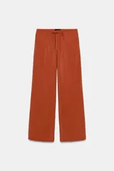 Pantalón tipo palazzo de corte recto y tejido fluido, color naranja. Presenta cintura elástica con cordón ajustable y bolsillos laterales.