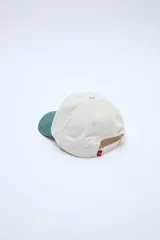 Gorra clásica con diseño en bloque de color, cuerpo en tono beige y visera en verde. Cuenta con bordado frontal con la palabra 'UNIFORM'.