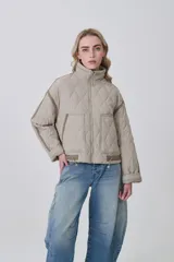 Campera acolchada de diseño capitoné en color beige, con cuello alto, cierre frontal y bolsillos laterales. Presenta un corte holgado con detalles de costuras reforzadas en las mangas y ajuste en la cintura.