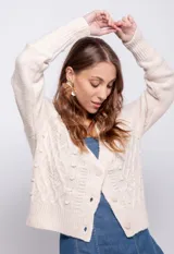 Cardigan de tejido de punto color beige, con diseño de ochos y puntos texturizados, cierre frontal de botones a tono y mangas largas con puños acanalados.