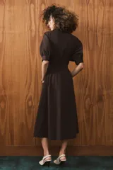 Vestido midi de algodón con cuello solapa, cierre frontal con botones y mangas cortas abullonadas con puños. Presenta un diseño evasé con bolsillos laterales ocultos y elástico en la espalda.