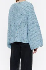 Jersey negro de punto con hilos de colores entretejidos, corte recto, escote barco y mangas largas abullonadas.