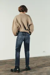 Jeans de tiro alto color marrón oscuro con acabado lavado, corte recto/flare y bajo cropped sin costuras. Presenta cinco bolsillos y cierre frontal con cremallera y botón metálico.