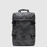 Mochila de viaje con diseño rectangular y estampado camuflado en tonos grises. Cuenta con correas laterales ajustables con hebillas plásticas, asa superior reforzada y bolsillo frontal con etiqueta de marca. Fabricada con material resistente y repelente al agua.
