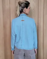 Camisa de denim con cuello alto tipo mao con volados, cierre frontal con botones y mangas largas con puños elásticos con volados.