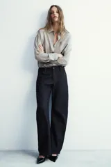 Camisa fluida de corte oversize confeccionada en mezcla de viscosa, con diseño de rayas verticales finas en tono beige sobre fondo blanco. Presenta cuello solapa, cierre frontal con botones, manga larga con puños y un bolsillo de plastrón en el pecho.
