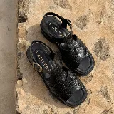 Sandalias de cuero vacuno negro con textura símil cocodrilo, diseño de tiras cruzadas, suela track de goma y hebilla metálica de ajuste en el tobillo.