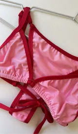 Conjunto de bikini de dos piezas, color rosa con ribetes rojos. El corpiño es de corte triangular con tirantes finos y la bombacha es de corte clásico con lazos laterales.