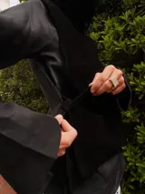 Chaleco negro de gamuza con cuello de pelo sintético y diseño estructurado, con lazos laterales para ajuste.