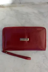 Billetera tipo sobre con correa de muñeca, confeccionada en cuero con textura de reptil en color marrón. Cuenta con cierre perimetral y placa metálica con el logo de la marca en el frente.