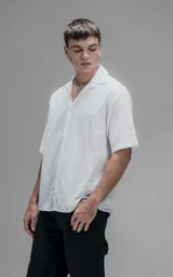 Camisa oversize blanca de manga corta y cuello abierto, confeccionada en algodón con diseño bordado.