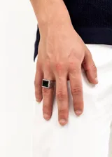 Anillo plateado de aleación de metales con piedra negra cuadrada en el centro.