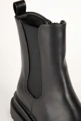 Bota Chelsea de cuero sintético color negro, con elástico lateral, puntera redondeada con detalle de perforaciones y suela track.