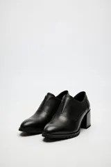 Zapato de cuero color beige, con taco de madera y suela dentada. Presenta un diseño slip-on con detalles de textura en relieve en los laterales y el empeine.