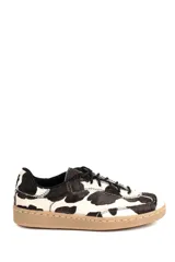 Championes de estilo urbano con diseño de manchas tipo vaca, confeccionados en cuero con textura de pelo. Presentan cordones negros, suela plana de goma en tono tostado y costuras reforzadas en el contorno.