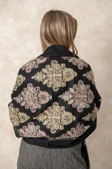 Pashmina de tela densa y suave, con caída pesada y diseño bordado con motivos florales en tonos dorados y beige. Presenta terminaciones con flecos en los extremos.