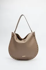 Bolso hobo grande color beige, de cuero sintético con textura suave. Tiene correa de hombro y detalle de tachas metálicas doradas en los bordes.