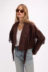 Chaqueta de efecto gamuza en color marrón, con solapas amplias, cierre frontal con botón y flecos largos decorativos en la parte frontal y trasera. Presenta un diseño estructurado de estilo western.