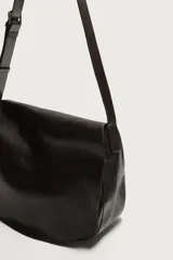 Bolso bandolera de piel color marrón oscuro, con diseño flexible y solapa frontal. Cuenta con asa larga ajustable y compartimento principal con bolsillo interior con cierre.