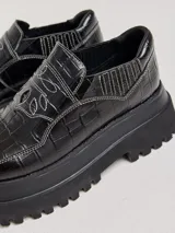 Mocasines color marrón con estampado de cocodrilo y plataforma negra con suela dentada.