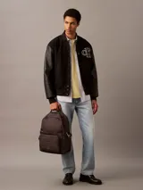 Mochila de poliéster reprocesado color gris oscuro/negro, con asa de mano superior y correas de hombro acolchadas. Presenta doble compartimento principal con cremallera, doble bolsillo exterior frontal con cremallera y parche con logotipo en la parte delantera.