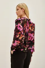 Camisa de viscosa con estampado floral en tonos fucsia, violeta y naranja sobre fondo negro. Presenta cuello con lazo ajustable y mangas largas con puños elásticos.