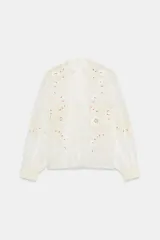 Camisa de organza de viscosa color crudo, con cuello subido, escote en V y manga larga. Presenta detalles de bordados florales en contraste a lo largo del frente y cierre frontal con botones.