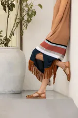 Vestido tejido en hilado de algodón con flecos de gamuza color tostado, con rayas horizontales en el ruedo en tonos negro, blanco, ladrillo y celeste.