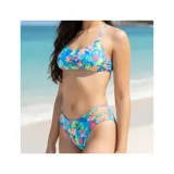 Bikini de dos piezas con estampado tropical de flores y hojas en tonos rosados, azules y verdes sobre fondo celeste. El corpiño es de diseño triangular con espalda cruzada, y la bombacha es cola less con tiras laterales decorativas.