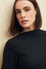 Top negro de textura acanalada con cuello semi alto y mangas largas. Presenta un diseño ajustado al cuerpo con una sutil abertura lateral en el ruedo.