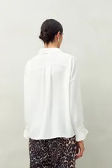 Camisa negra de manga larga con cuello clásico y botones frontales. El tejido presenta una textura arrugada o plisada, y los puños tienen un frunce elástico.