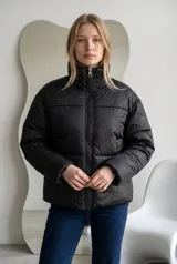 Campera puffer negra con diseño acolchado y pequeños detalles brillantes distribuidos por toda la prenda. Presenta cuello alto, cierre frontal completo y mangas largas.