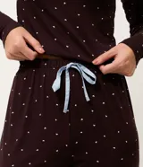 Conjunto de pijama compuesto por una remera de manga larga con cuello redondo y detalle de lazo, y un pantalón tipo jogger. Ambas piezas presentan un estampado de corazones pequeños sobre un fondo oscuro.